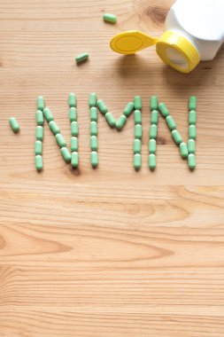 Nikotinamit mononükleotid, anti vitamin. Tahta zemin üzerinde NMN alfabesine biçim veren yeşil haplar, kopyalama alanı, üst görünüm.