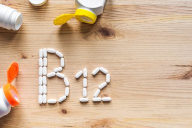  B12 vitamini. Tahta zemin üzerinde B12 alfabesine biçim veren yeşil haplar, kopyalama alanı, üst görünüm.