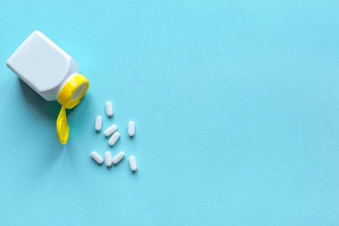 Mavi arka planda hap şişesi ve haplar, üst manzara, kopyalama alanı. İlaç ve eczane konsepti. Vitaminler veya genel haplar.