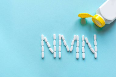 Nikotinamit mononükleotid, niasin, anti-etil vitamin. Mavi arkaplanda NMN alfabesine biçim veren beyaz haplar, boşluk kopyala, üst görünüm.