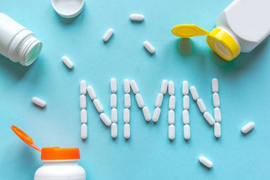 Nikotinamit mononükleotid, niasin, anti-etil vitamin. Mavi arkaplanda NMN alfabesine biçim veren beyaz haplar, boşluk kopyala, üst görünüm.