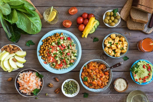 Vegan dinner table, set of healthy vegan vegetarian dishes for lunch - quinoa and chickpea salad, fried tofu, hummus dip, fruits, vegetables, nuts, seeds, top view, flat lay.