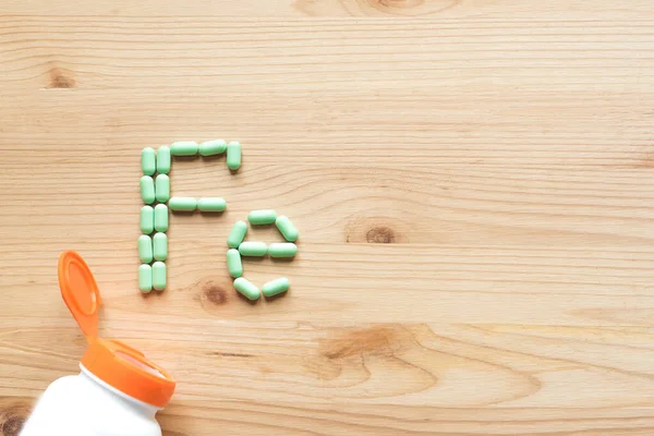 铁补充剂 贫血治疗 木制背景 顶视图 复制空间上形成Fe字母表的绿色药丸 — 图库照片