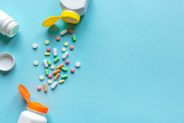 Bottles with various colorful pills, tablets on blue background, top view, copy space. Vitamins and generics, pharmacy and medicine concept.