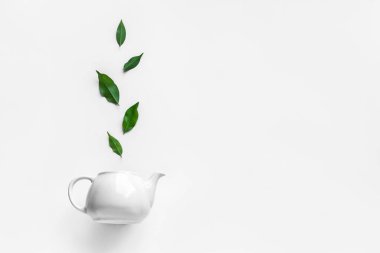 Yeşil Çay - beyaz çaydanlık ve beyaz arka planda çay yaprakları. Organik çay düzlüğü - fincan ve yeşil yapraklar, üst görünüm, kopyalama alanı.