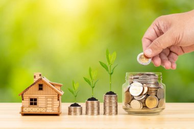 Bozuk para kavanozu ve büyüyen yapraklarla dolu yığın, ve ahşap masa üzerinde manken evi yeşil ağaç zemin, içine para koymak, ipotek konsepti