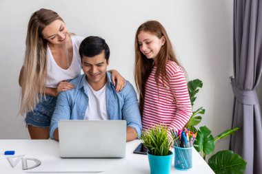 Erkek ya da baba evde bilgisayar kullanarak çalışıyor, kızıyla birlikte, anne tarafından kucaklanıyor.