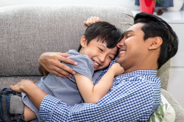 Mutlu Asyalı baba, oğluna sarıldı ve sarıldı. Oturma odasında kanepede uzandı. Aile bağı ve ilişki kavramı.