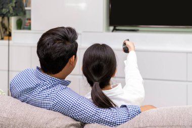Asyalı çiftin kanepede oturup uzaktan kumandayla televizyon izlemesinin keyfini çıkarırken.