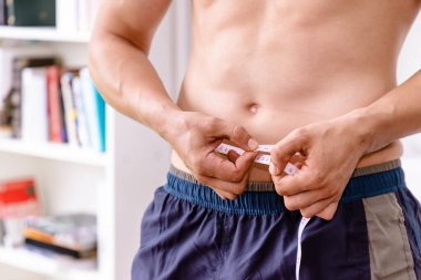 Ölçüm bandı, kilo kaybı ve diyet konsepti olan kaslı erkek gövdesi