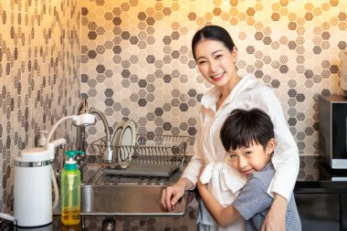 Güzel, genç, Asyalı erkek çocuk modern mutfak odasında kadına sarılıyor ve kameraya bakıyor.