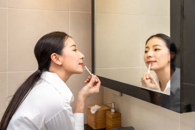 Güzel Asyalı kadın aynaya bakıyor ve tuvalette ruj sürüyor.