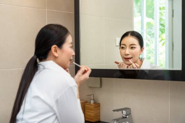 Güzel Asyalı kadın aynaya bakıyor ve tuvalette ruj sürüyor.