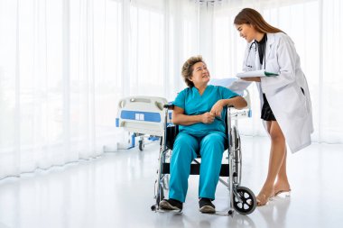 Asyalı doktor tekerlekli sandalyedeki yaşlı kadın hastayla ilgileniyor.