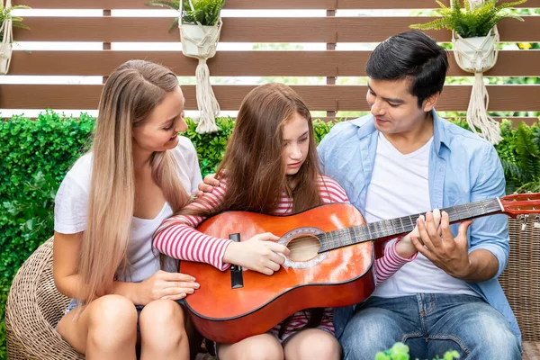 Happy family singing, and enjoy music in garden at house. Dad teaching daughter to play guitar,  family relationship concept.