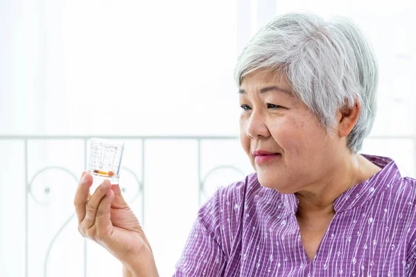 Senior elder woman female looking at measuring glass cup checking medicine