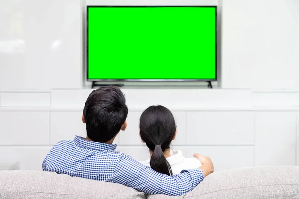 Asyalı bir çiftin kanepeye oturup yeşil ekranlı televizyon izlemesinin keyfini çıkarırken.