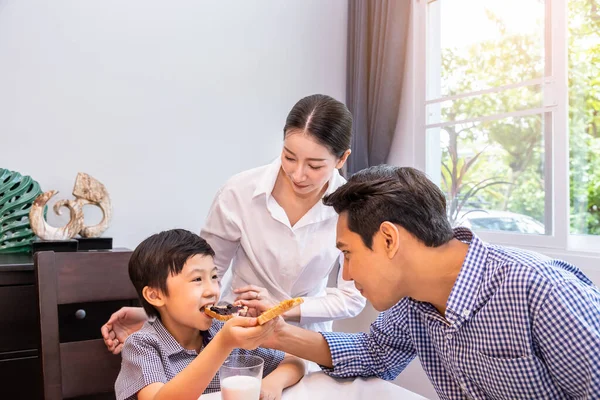 Happy Asian family in dining room, father feed bread to son boy, with mother