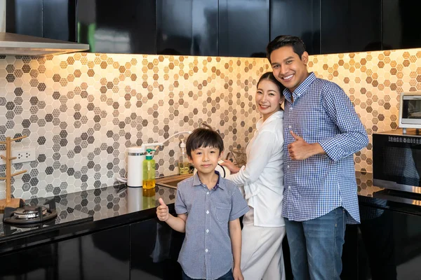 美しいです若いですアジアの女性の母親とともに男の夫と若い男の子の息子の家族現代的なキッチンルームで食器洗い機 カメラを見て 親指アップ — ストック写真