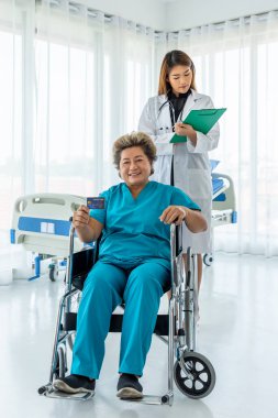 Tekerlekli sandalyedeki Asya 'lı yaşlı kadın hasta ayrıcalık ve ödeme için kredi kartını tıbbi doktorla birlikte gösteriyor.