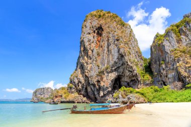 Uzun kuyruk teknesi ve turkuaz kristal berrak deniz suyu kireçtaşı uçurumu ve dağ Phra Nang Sahili, Krabi, Tayland