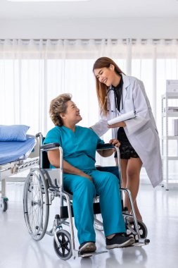 Asyalı doktor tekerlekli sandalyedeki yaşlı kadın hastayla ilgileniyor.