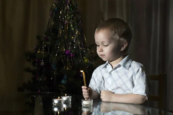 O pequeno rapaz acende velas em um contexto do abeto de Ano Novo Fotografia De Stock