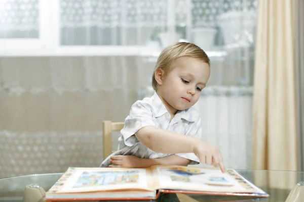 Παιδί εξετάζει το πρώτο βιβλίο του, κάθεται στο τραπέζι — Φωτογραφία Αρχείου