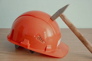 İş güvenliği, ev iyileştirme, onarım, inşaat ve onarım kavramı. Ahşap tezgahta portakal rengi güvenlik şapkası ve çekiç. Koruyucu bir miğfere çekiç darbesi. Çekiç sesi