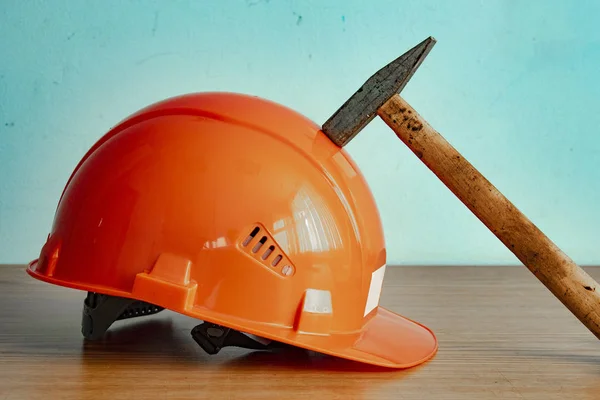 Concept of labor safety, home improvement, repair, construction and repair.Orange safety hat and hammer on wooden counter table.  Hammer blow on a protective construction helmet. Hammer beat