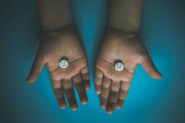 Gülen suratlı haplar. Antidepresan ve iyileşme konsepti. Çocuk hap alıyor, elinde beyaz bir tablet tutuyor. İlaç, antidepresan veya vitamin kavramı