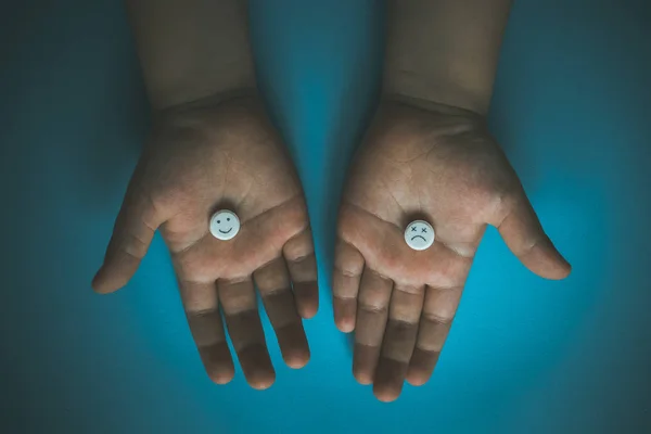 Gülen suratlı haplar. Antidepresan ve iyileşme konsepti. Çocuk hap alıyor, elinde beyaz bir tablet tutuyor. İlaç, antidepresan veya vitamin kavramı