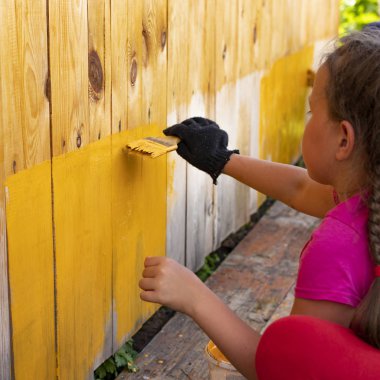 Bir kız eli bir fırçayla duvarı boyuyor. Sarı arkaplan
