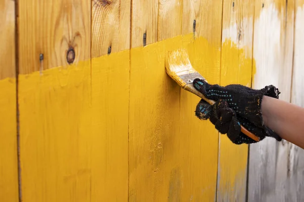 close up in gloves painting a wood wall in the yellow. Renovation.creative design house renovation theme. How to Paint Wooden Surface. Selected focus