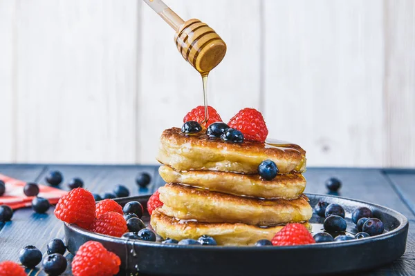 Pancakes with honey and berries on a wooden table