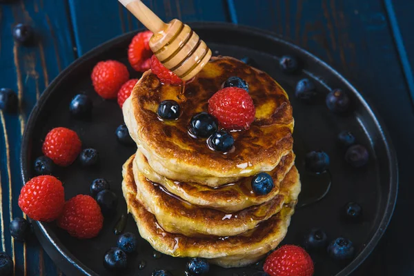 Pancakes with honey and berries on a wooden table