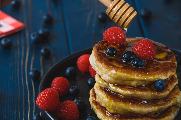 Pancakes with honey and berries on a wooden table