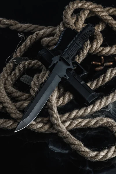 Solders combat knife smoke rope and gun on black background