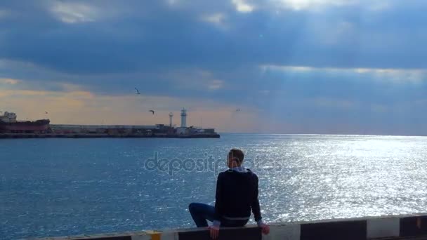 Der Kerl sitzt auf der Anklagebank und bewundert das Meer — Stockvideo
