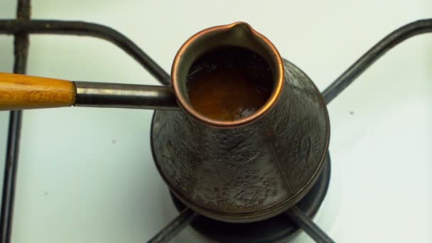Turkse koffie maken in koperen cezve boven gasfornuis. Op het gasfornuis Turk met een lopende koffie. Koffie van dichtbij zetten. Koffie in een cezve op een gasfornuis begint te koken. — Stockvideo
