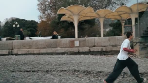 Los chicos realizan acrobacias en la playa de otoño. El tipo está entrenando a Parkour. Salta sobre la barandilla en un frío día de otoño. Hace una voltereta. Inteligentemente saltando. Parkour. . — Vídeo de stock