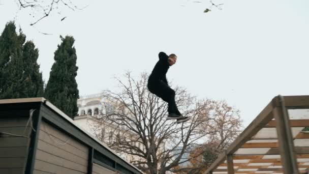 男は夏の木製のバーの屋根に屋根からジャンプします。奴は訓練場だ寒い秋の日に手すりにジャンプします。裏返しをするかなりジャンプしてる駐車場. — ストック動画
