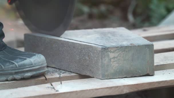 Beton snijmachine. Een arbeider in het parkgebied snijdt zware platen voor een loopbrug in het park. Werkt overdag beton snijden in het park. Veel stof verstrooit.. 4k — Stockvideo