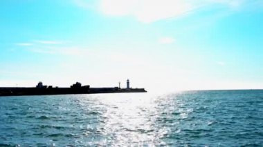 Parlak güneşli bir kış günü deniz parlayan bir deniz fenerinin arka planında. Denizde güneşli tavşanlar. Sakin, güzel hava, güzel manzara. 4k