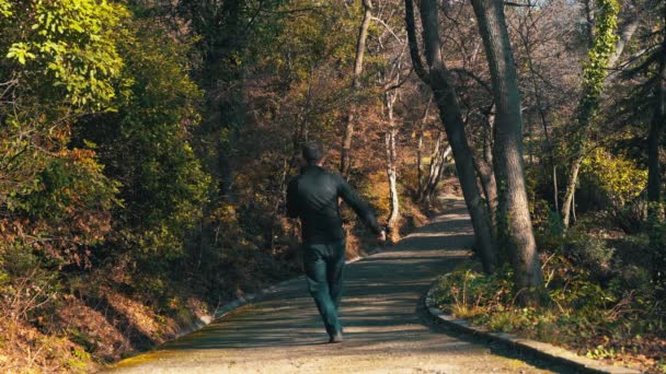 Samotny człowiek spaceruje zimą po parku w słoneczny dzień, słucha muzyki ze słuchawkami i zaczyna tańczyć głupio i wesoło. Mężczyzna aktywnie tańczy w parku słuchając muzyki na — Wideo stockowe