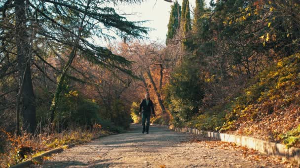 A lonely man walks in the park in the winter on a sunny day, listens to music with headphones and starts dancing stupidly and cheerfully. A man is actively dancing in the park listening to music on — Stockvideo