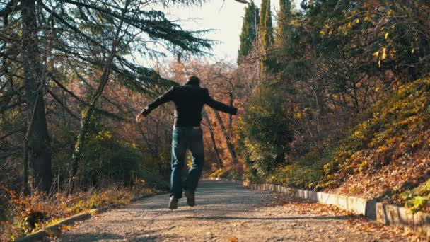 Un hombre solitario camina en el parque en invierno en un día soleado, escucha música con auriculares y comienza a bailar estúpida y alegremente. Un hombre está bailando activamente en el parque escuchando música en — Vídeos de Stock