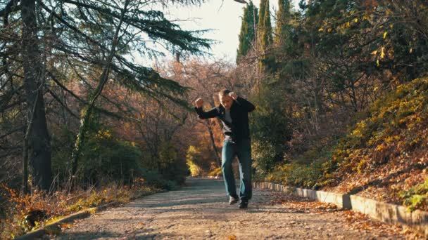 Un hombre solitario camina en el parque en invierno en un día soleado, escucha música con auriculares y comienza a bailar estúpida y alegremente. Un hombre está bailando activamente en el parque escuchando música en — Vídeos de Stock