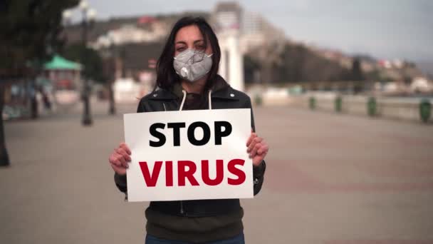 Mädchen Nahaufnahme in der Stadt ist in einer medizinischen Maske mit einem Plakat STOP VIRUS — Stockvideo