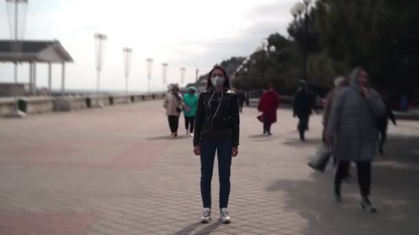 У місті стоїть дівчина у медичній масці. Люди швидко біжать повз неї. — стокове відео
